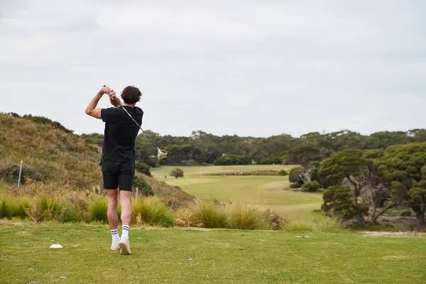 A golfer tees off toward a coastal fairway